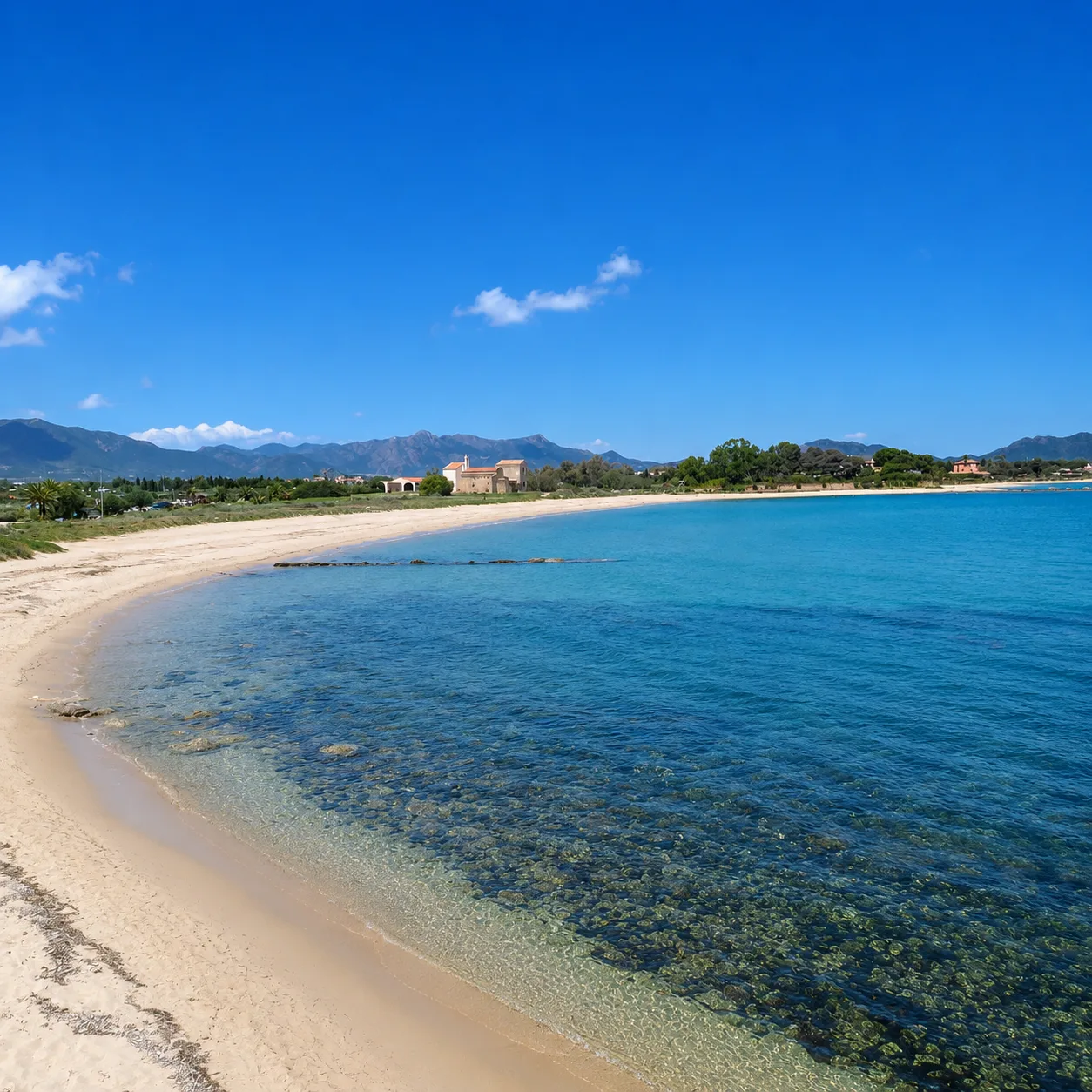 Spiaggia di Nora, Pula — arenile dorato con mare limpido e antica chiesa sullo sfondo