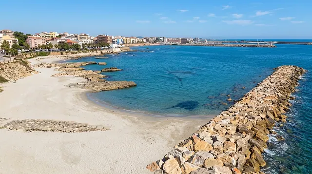 Acque Dolci, Porto Torres — piccola baia urbana di sabbia chiara con frangiflutti in pietra e acqua limpida turchese