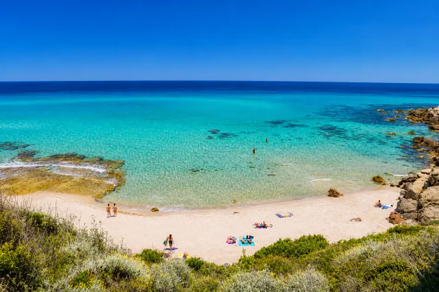 Ampurias, Castelsardo — caletta sabbiosa con acqua trasparente, scogli dorati e macchia mediterranea