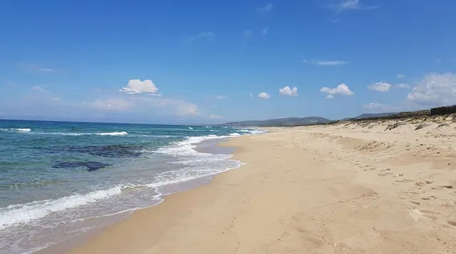 Baia delle Mimose, Badesi — lunga spiaggia sabbiosa con dune, mare aperto con onde leggere e profilo costiero all'orizzonte