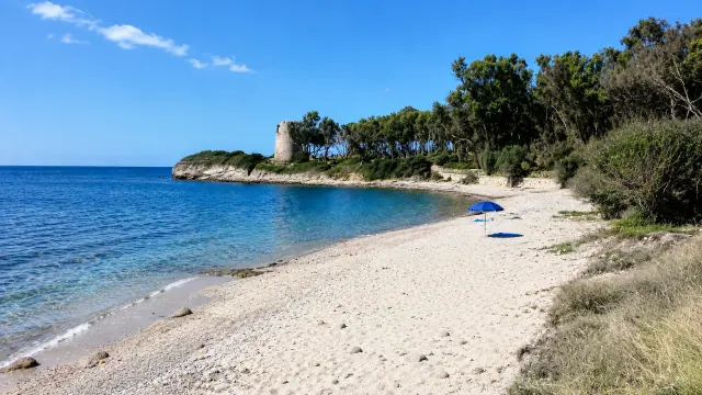 Cala d'Ostia, Pula — piccola cala con torre costiera, pini e acqua azzurra