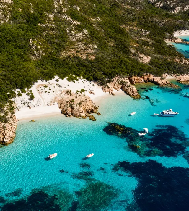 Cala Soraya, Caprera — vista dall'alto su piccole cale di sabbia chiara con mare turchese e barche ferme in rada