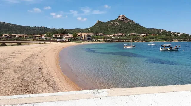 Cannigione, Arzachena — spiaggia del paese con sabbia dorata, mare calmo trasparente e barche da pesca ormeggiate
