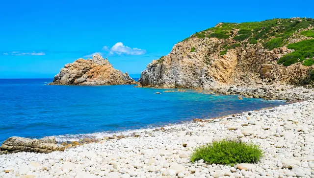 Capo Pecora, Arbus — caletta di ciottoli bianchi con scogli granitici, mare blu intenso e macchia mediterranea sulla scogliera