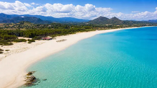 Costa Rei, Muravera — lunghissima spiaggia chiara con mare turchese e rilievi sullo sfondo