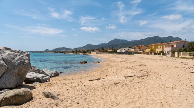 Frutti d'Oro, Capoterra — spiaggia sabbiosa con grossi massi granitici, case colorate e il profilo delle montagne alle spalle