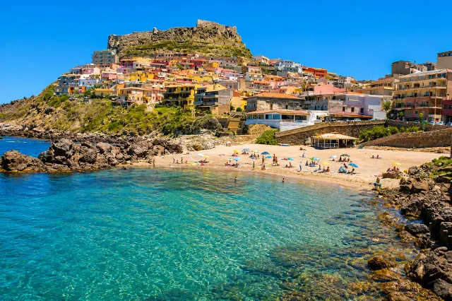Lu Bagnu, Castelsardo — spiaggia urbana ai piedi del borgo colorato con castello sul promontorio e mare cristallino