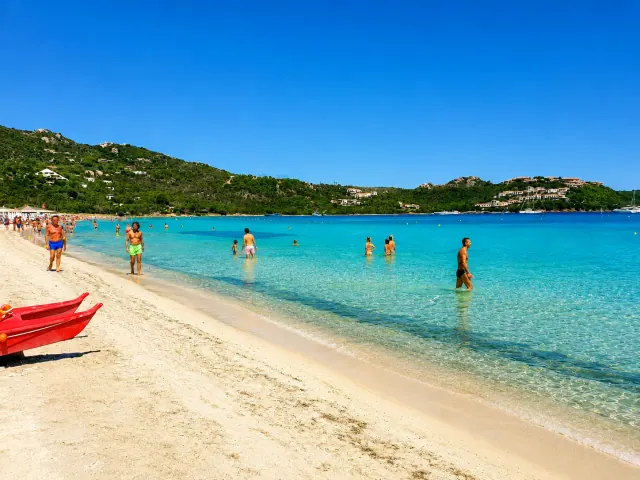 Marinella, Olbia — lunga spiaggia di sabbia chiara con mare turchese cristallino e bagnanti nella baia riparata