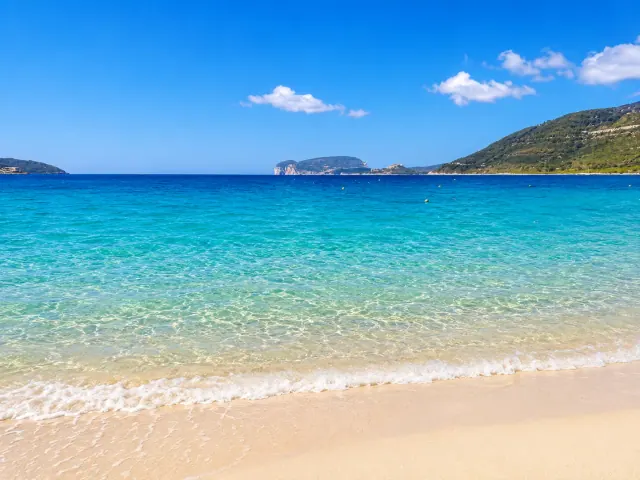 Mugoni, Alghero — baia di Porto Conte con sabbia dorata, acqua trasparente e Capo Caccia sullo sfondo