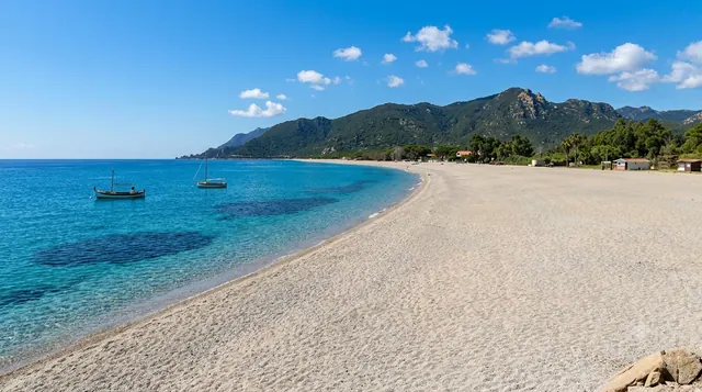 Museddu, Cardedu — lunga curva di sabbia chiara con mare limpido e montagne sullo sfondo