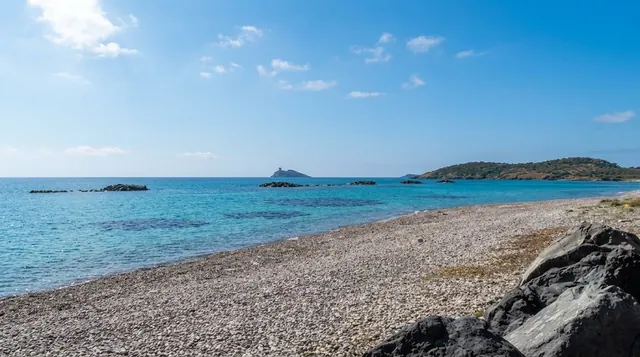 Perd'e Sali, Sarroch — spiaggia di ciottoli chiari con acqua azzurra trasparente, scogli affioranti e isolotto con torre all'orizzonte