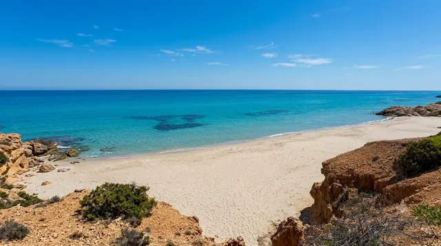Pinus Village, Pula — caletta di sabbia chiara tra rocce ocra e macchia mediterranea, con mare turchese trasparente