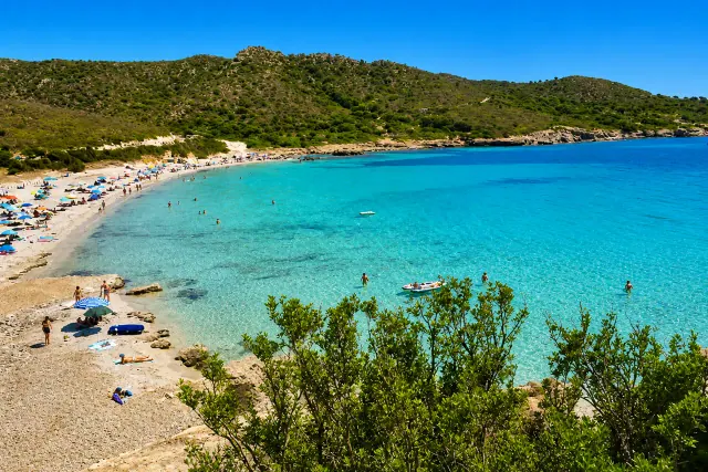 Piscinnì, Teulada — cala riparata con sabbia chiara, acqua turchese cristallina e collina coperta di macchia mediterranea