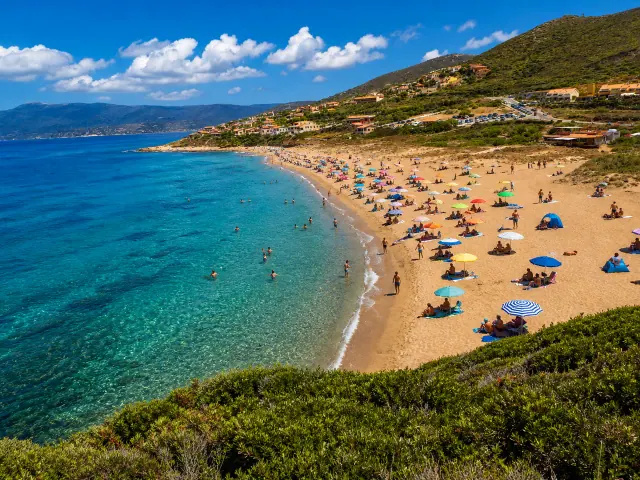 Porto Alabe, Tresnuraghes — lunga spiaggia dorata con acqua turchese e case sul versante collinare