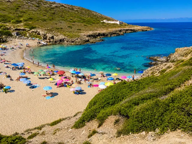 Porto Palmas, Sassari — cala sabbiosa tra rocce e macchia mediterranea con mare blu intenso