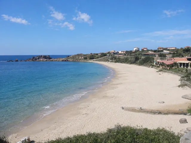 Portopaglietto, Portoscuso — ampia mezzaluna di sabbia chiara con acqua limpida e case del paese affacciate sulla baia
