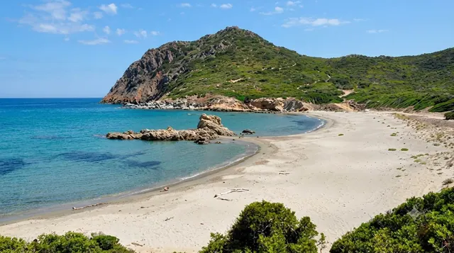 Portu s'Ilixi, Muravera — baia riparata con sabbia chiara, promontorio verde, scogli affioranti e acqua turchese trasparente