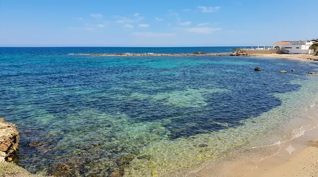 Scogliolungo, Porto Torres — acqua trasparente su fondale roccioso e sabbioso con litorale urbano sullo sfondo