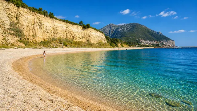 Sos Dorroles, Dorgali — cala di ciottoli chiari sotto la falesia con acqua turchese cristallina
