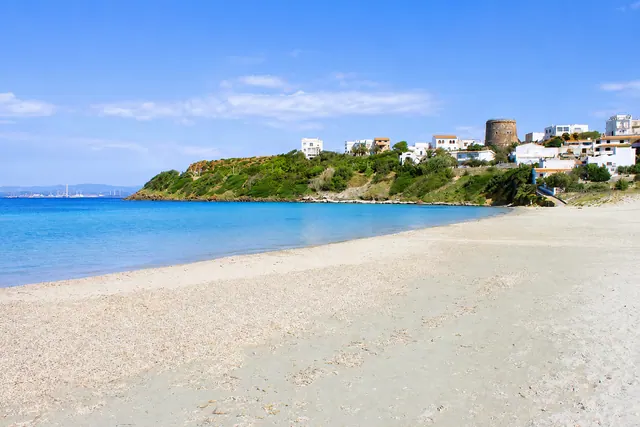 Sottotorre, Calasetta — spiaggia di sabbia chiara con baia riparata, acqua turchese e torre aragonese sul promontorio con le case bianche