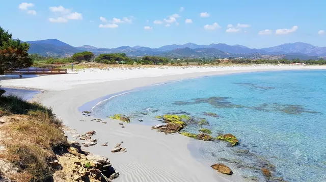 Spiaggia di Sant'Anna, Budoni — mezzaluna di sabbia chiara con acqua turchese poco profonda e montagne sullo sfondo